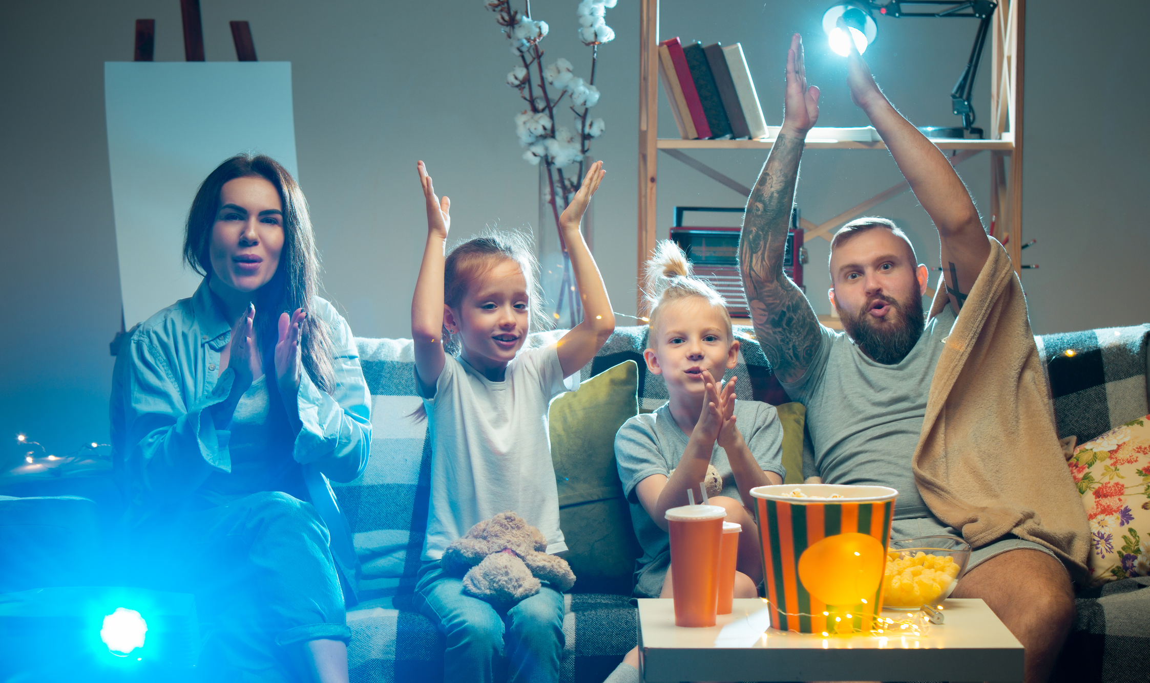 Happy family watching projector, TV, movies with popcorn in the evening at home. Mother, father and kids spending time together.